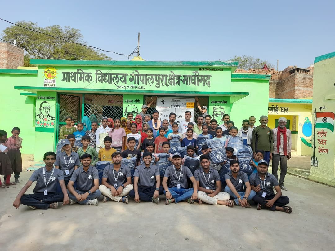 Helping Hut volunteers sit and stand for a large group photo with children and residents outside the green-painted Gopalpura primary school building.