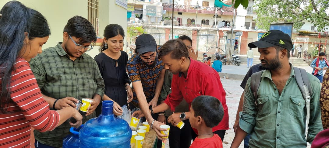 Helping Hut volunteers gathered around a table with a water jug and cups hand a cold drink to a young boy on the street.