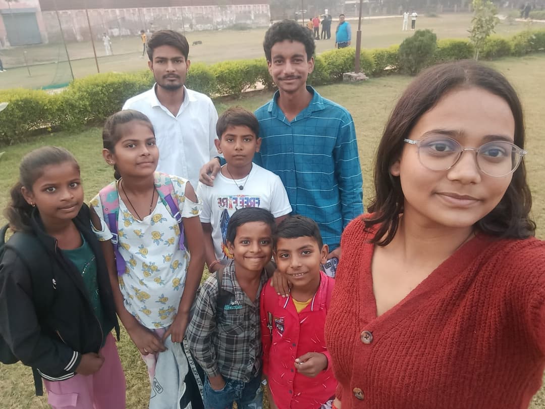 Helping Hut volunteers take a cheerful group selfie with Udaan Street School students on a park lawn.
