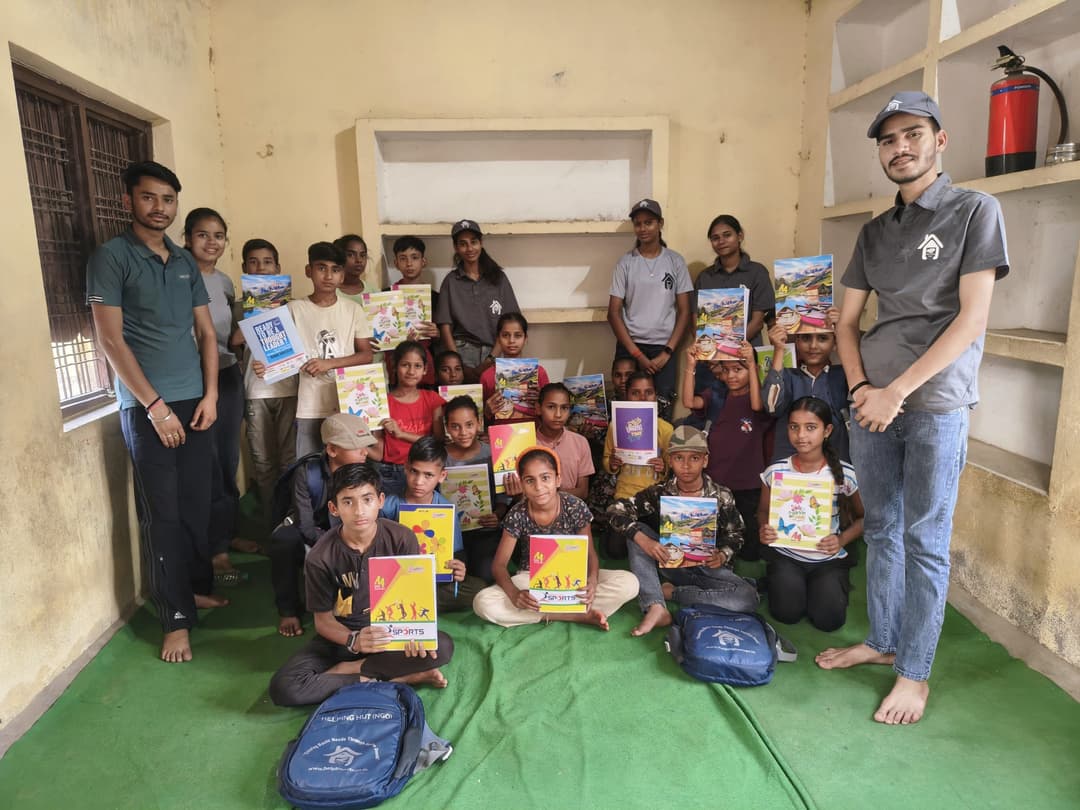 Udaan Street School students hold up their new notebooks alongside Helping Hut volunteers during a study material distribution in the classroom.