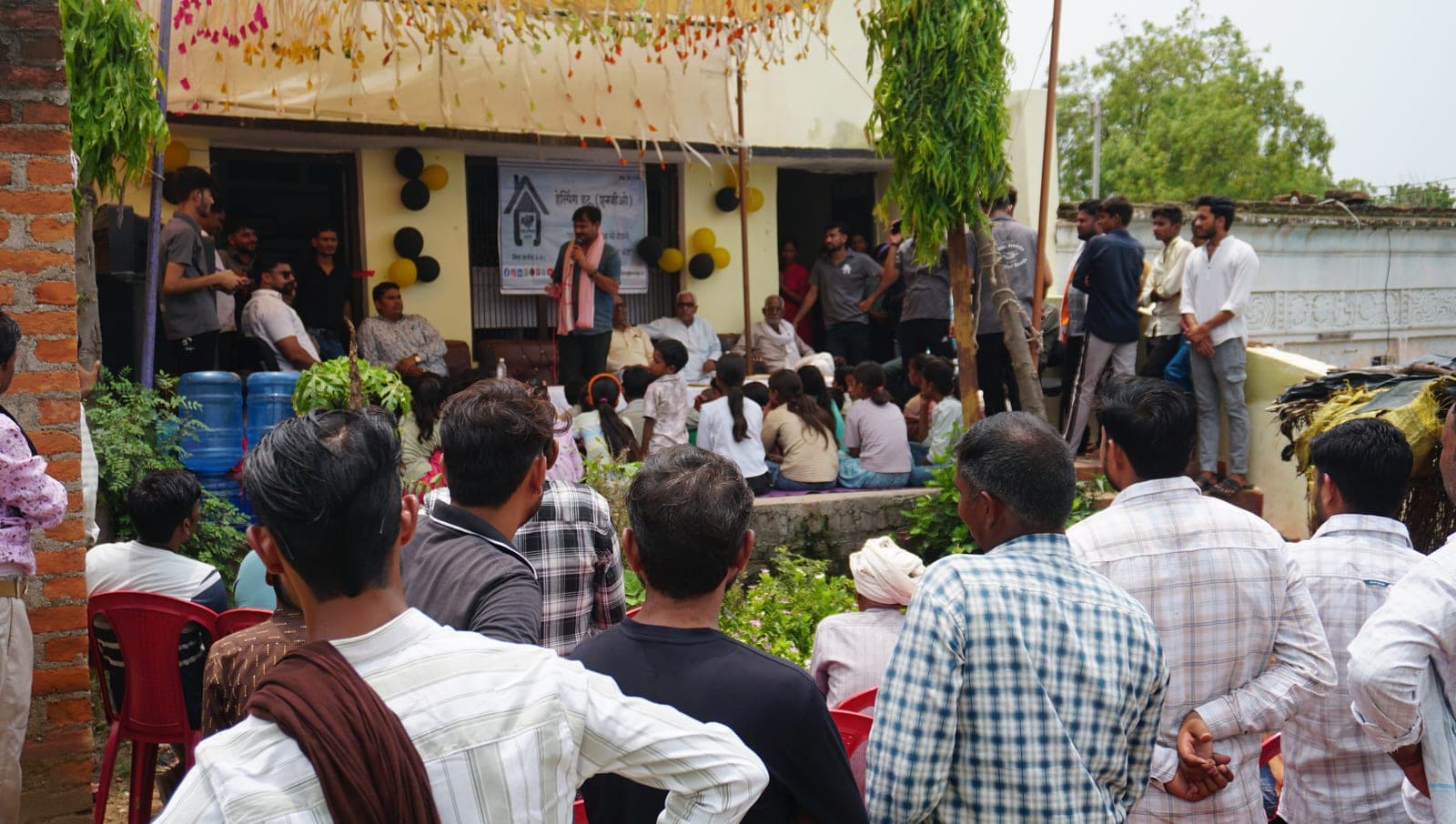 A Helping Hut volunteer addressing villagers and children gathered at the inauguration ceremony