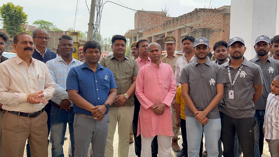 Helping Hut volunteers in grey uniforms stand alongside local officials, police personnel and village elders at a community gathering in Gopalpura.