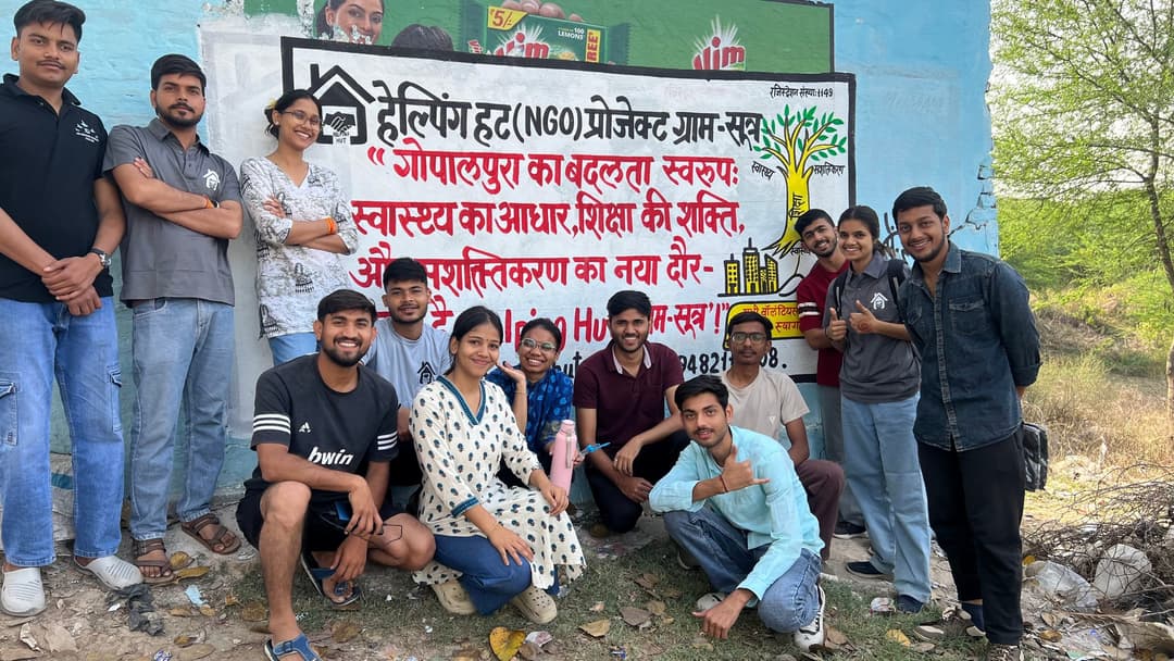 Helping Hut volunteers give thumbs up around a freshly painted wall mural announcing Project GramSutr and its message of health, education and empowerment for Gopalpura.