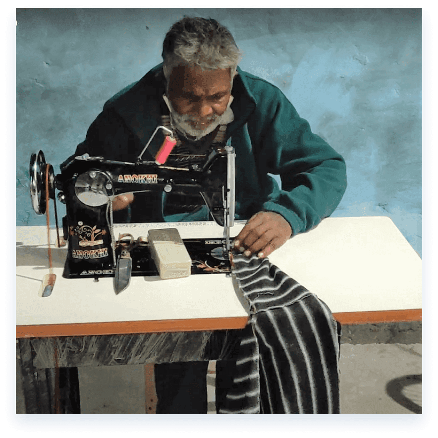 A tailor working at a hand-operated sewing machine, guiding striped cloth under the needle.