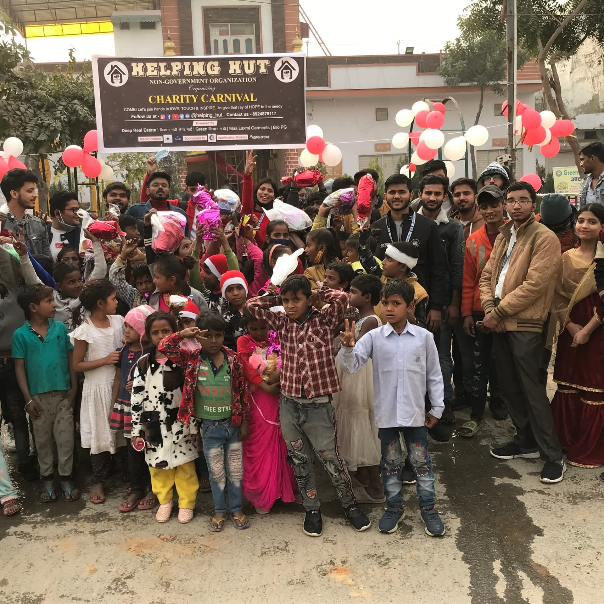 Helping Hut volunteers and local children gathered under the Charity Carnival banner in Dwarka