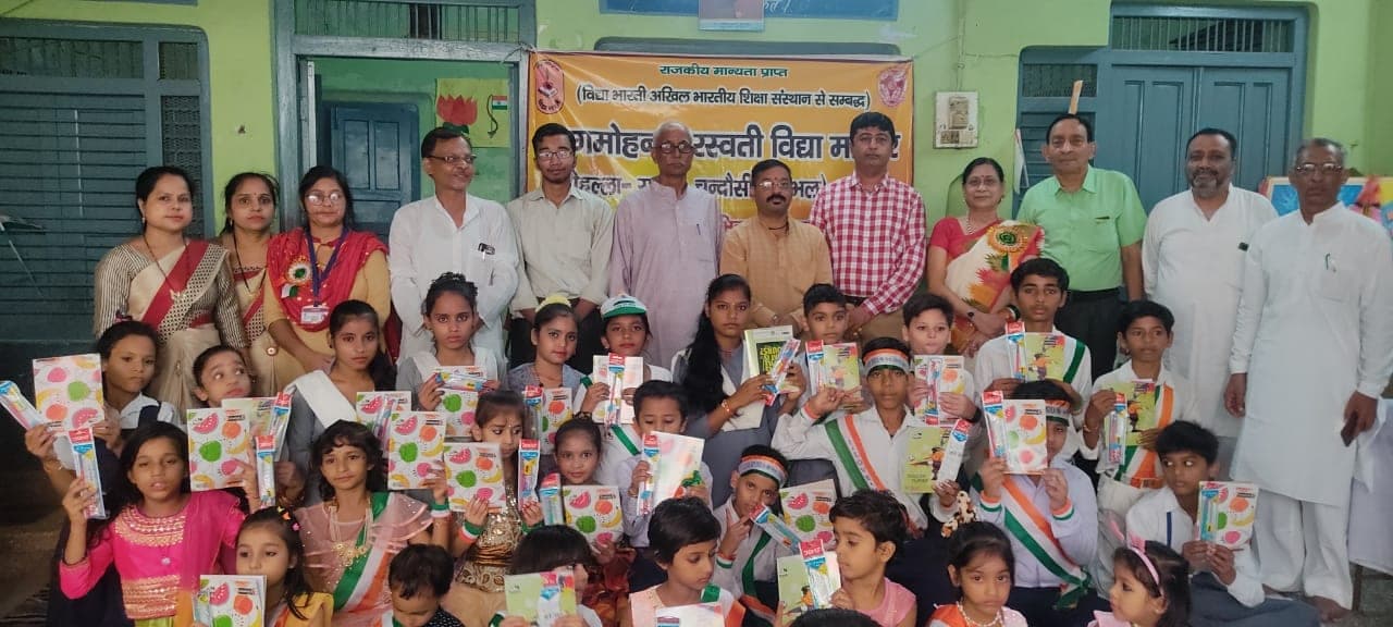 Helping Hut volunteers and teachers with schoolchildren holding stationery kits at a school distribution event in Chandausi