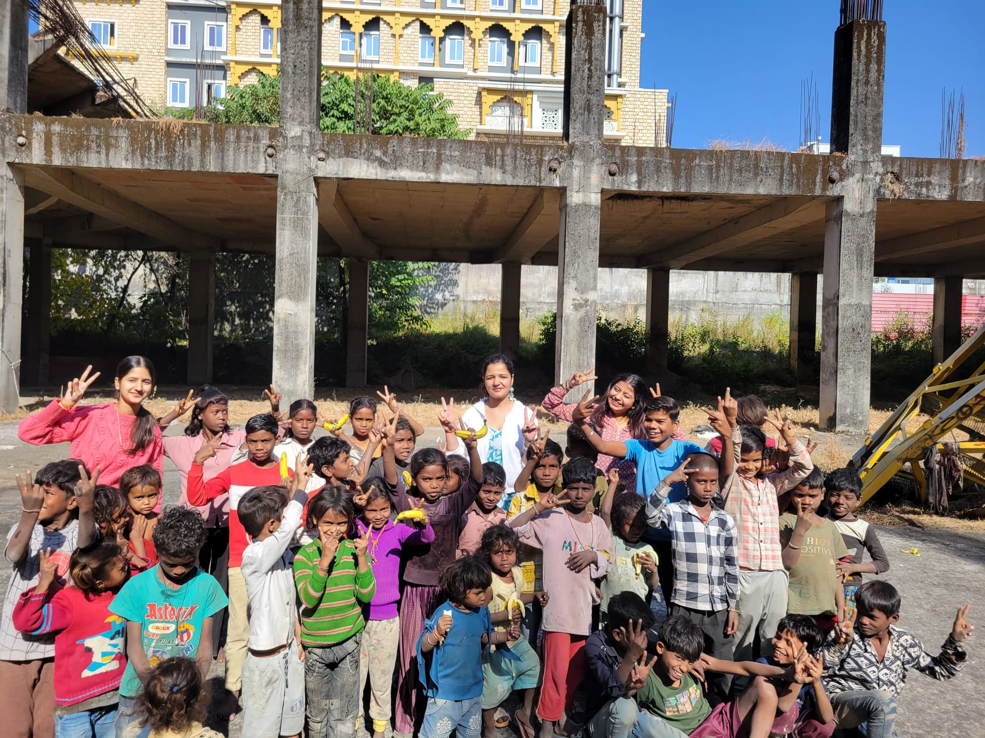 Helping Hut volunteers and children flashing victory signs during a snack distribution outreach at a construction site in Dehradun