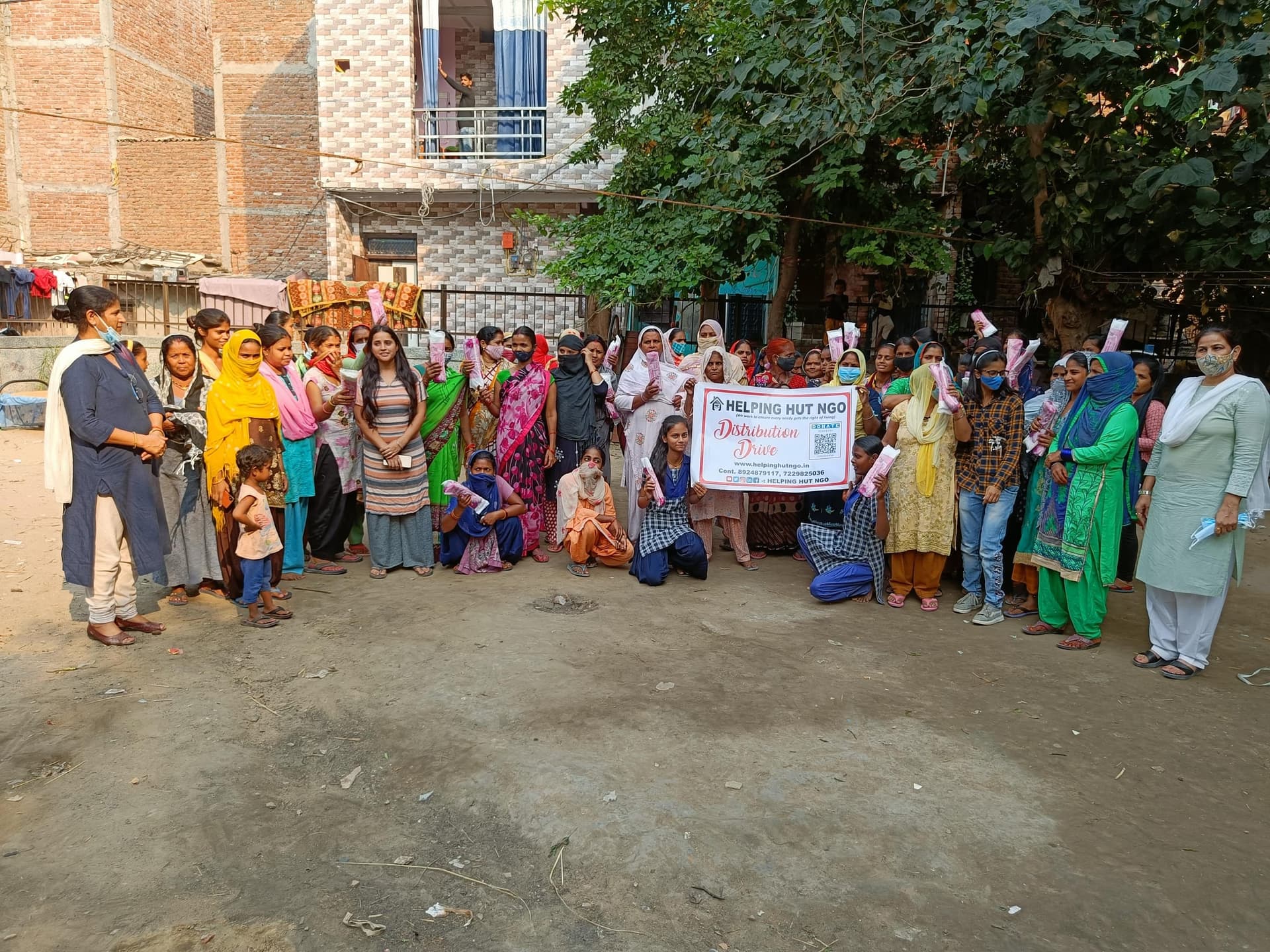Helping Hut volunteers holding a Helping Hut NGO distribution drive banner with a large group of local women at a community distribution event in Delhi