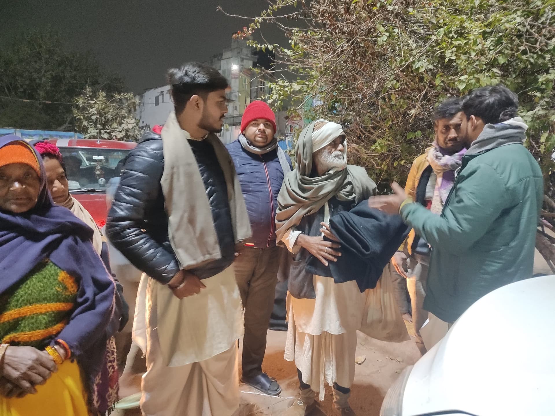 Helping Hut volunteers giving a blanket to an elderly woman on the street during a winter night distribution drive in Etawah