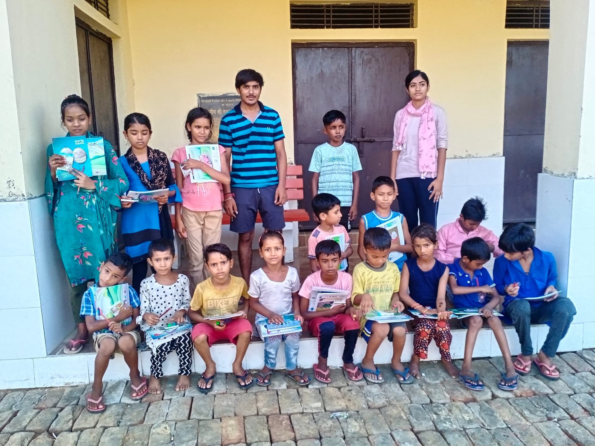 Helping Hut volunteers with children displaying notebooks and study materials at an outdoor learning session in Faridabad