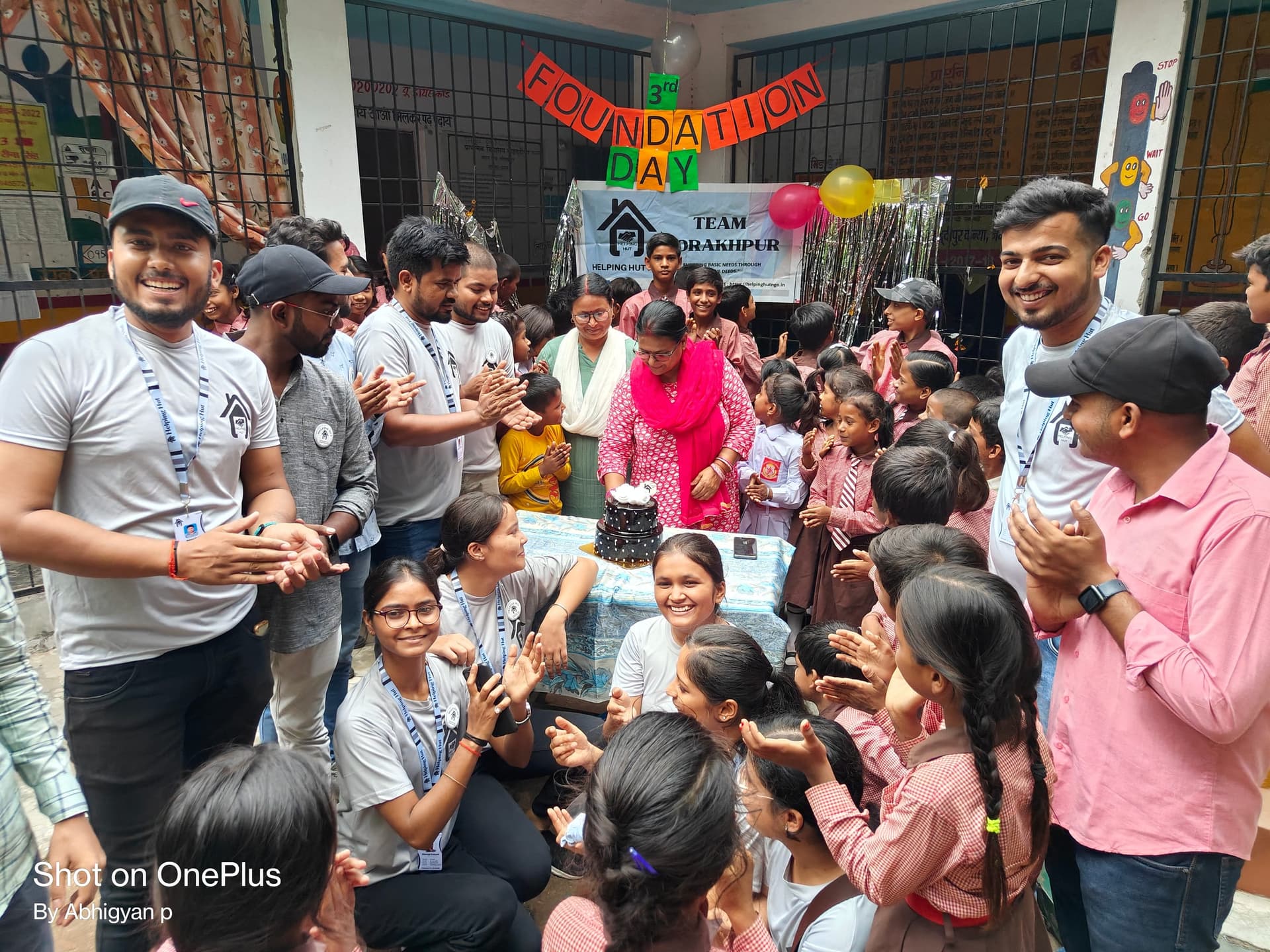 Helping Hut volunteers in team T-shirts celebrating the NGO's third Foundation Day with schoolchildren under a Team Gorakhpur banner