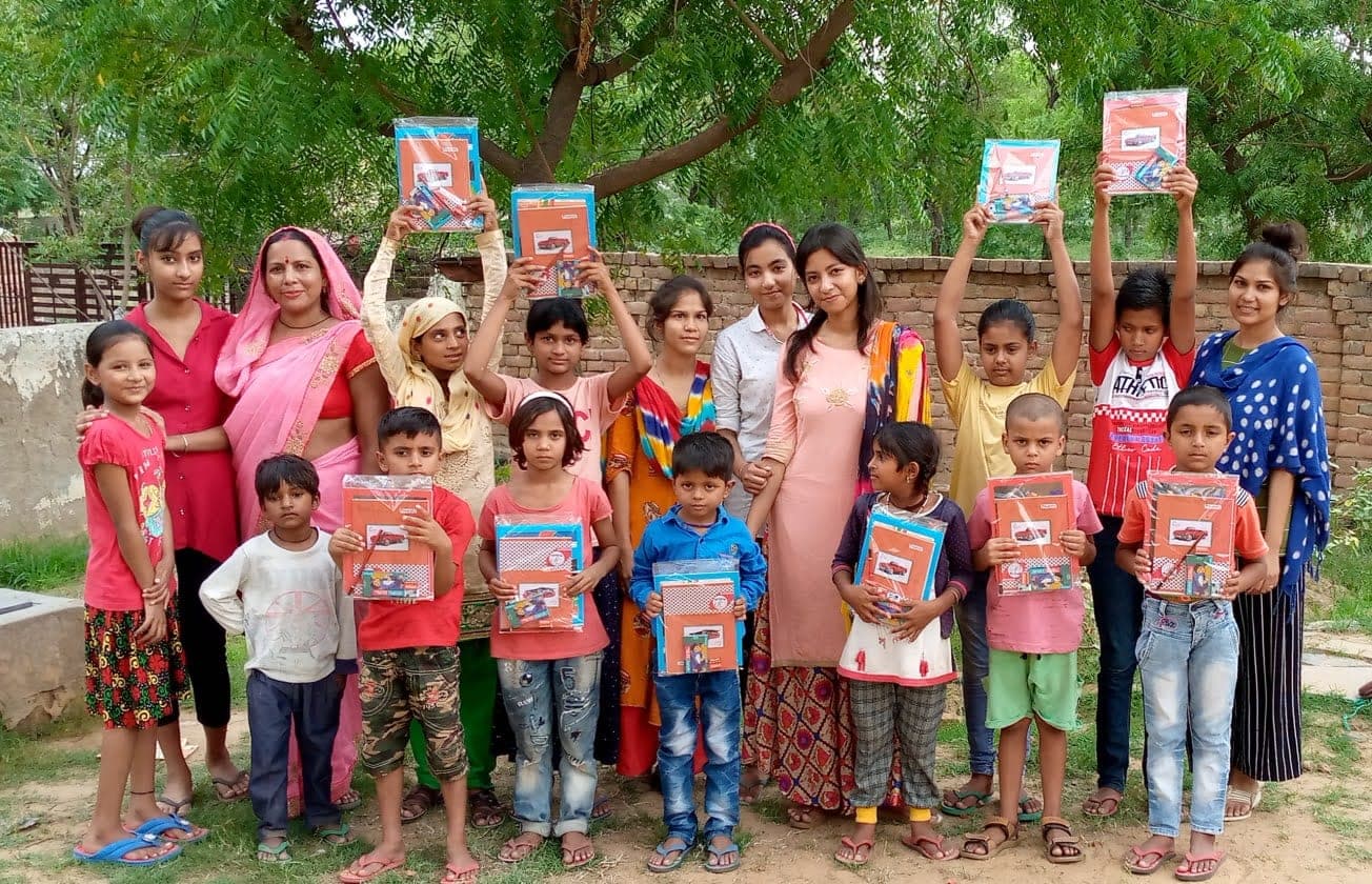 Helping Hut volunteers and village children holding up donated notebook and stationery kits outdoors in Kota