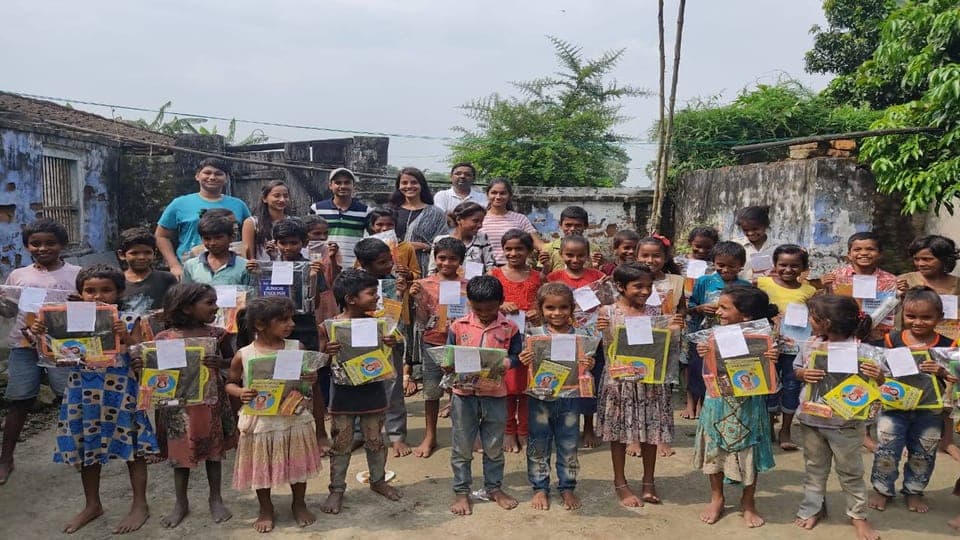 Helping Hut volunteers with village children holding up notebooks and stationery kits in Samastipur